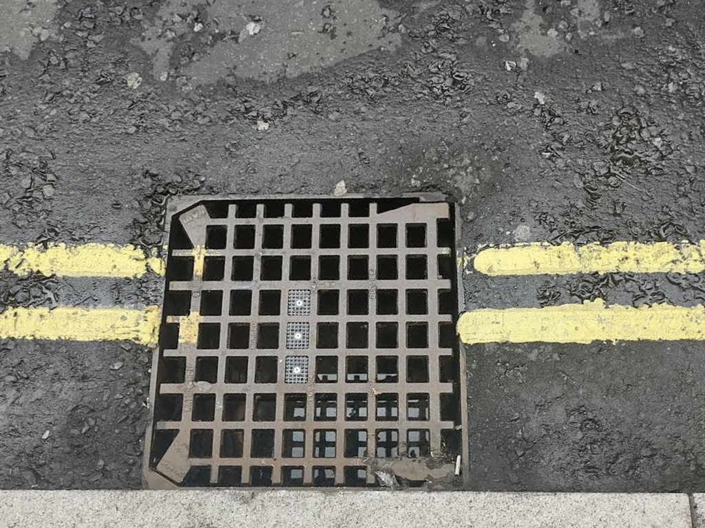 An image of a UDlive Retrofit Drain Sensor installed on an existing grate.